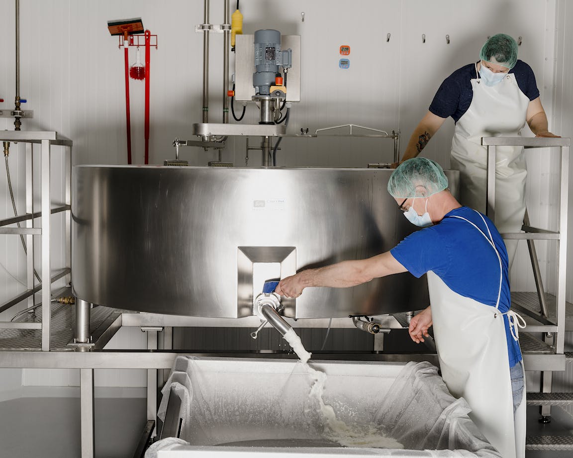 A person works on industrial cheesemaking equipment.